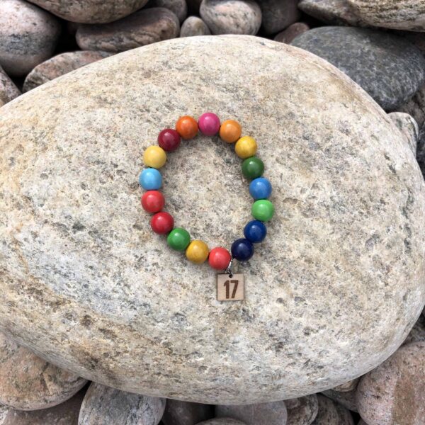 Armband med färgglada träpärlor, som ligger på en sten.